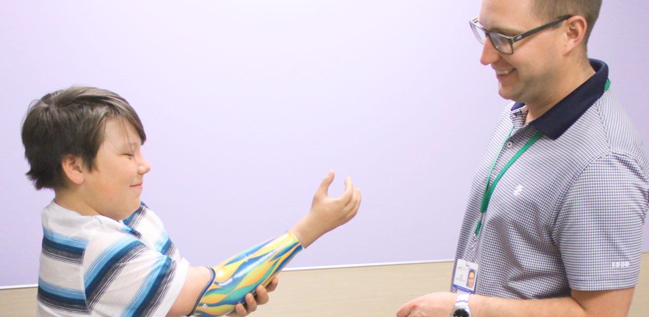 tween boy trying on prosthetic arm in front of physical therapist