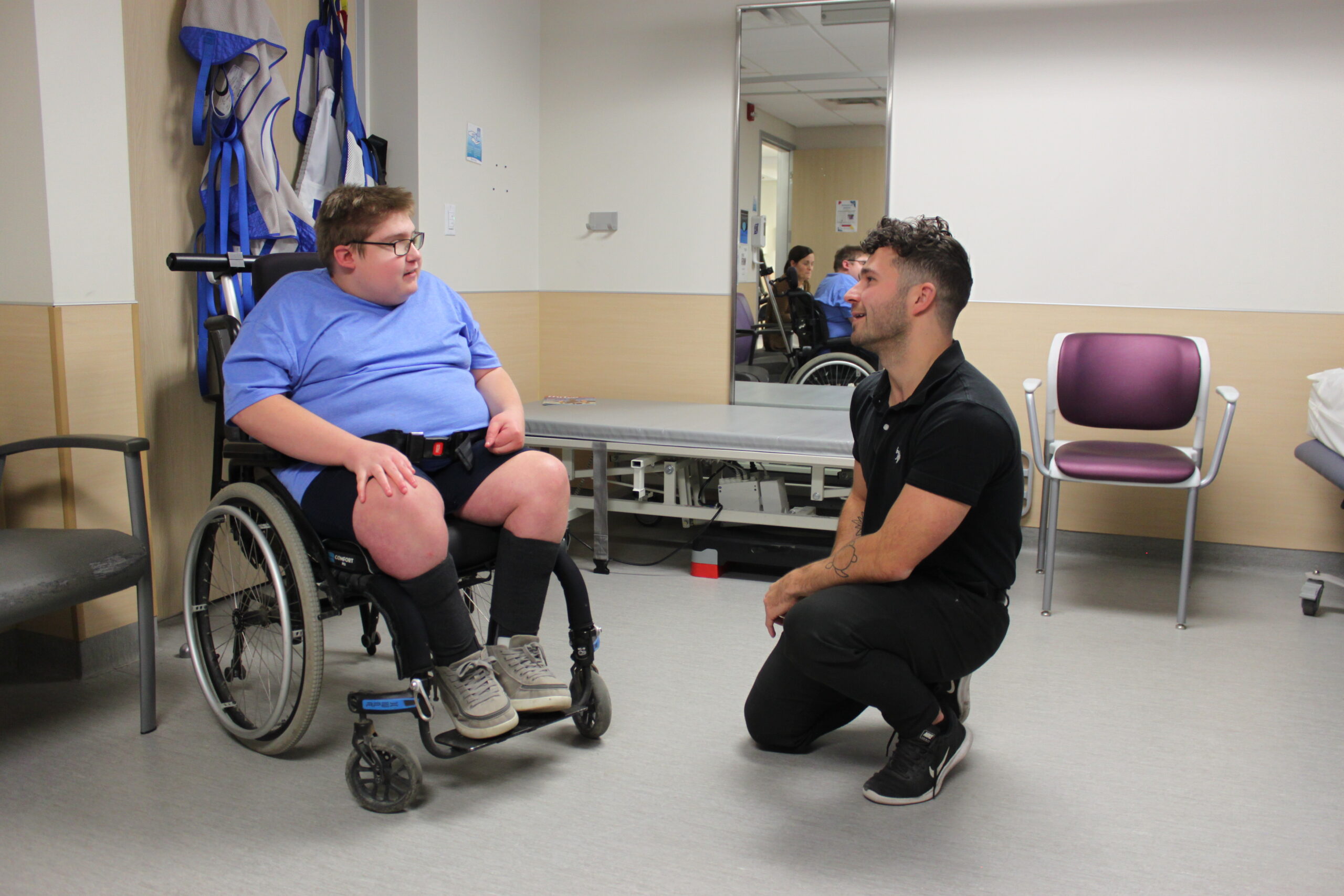 Boy in wheelchair speaks with therapist who is crouched infront of him.