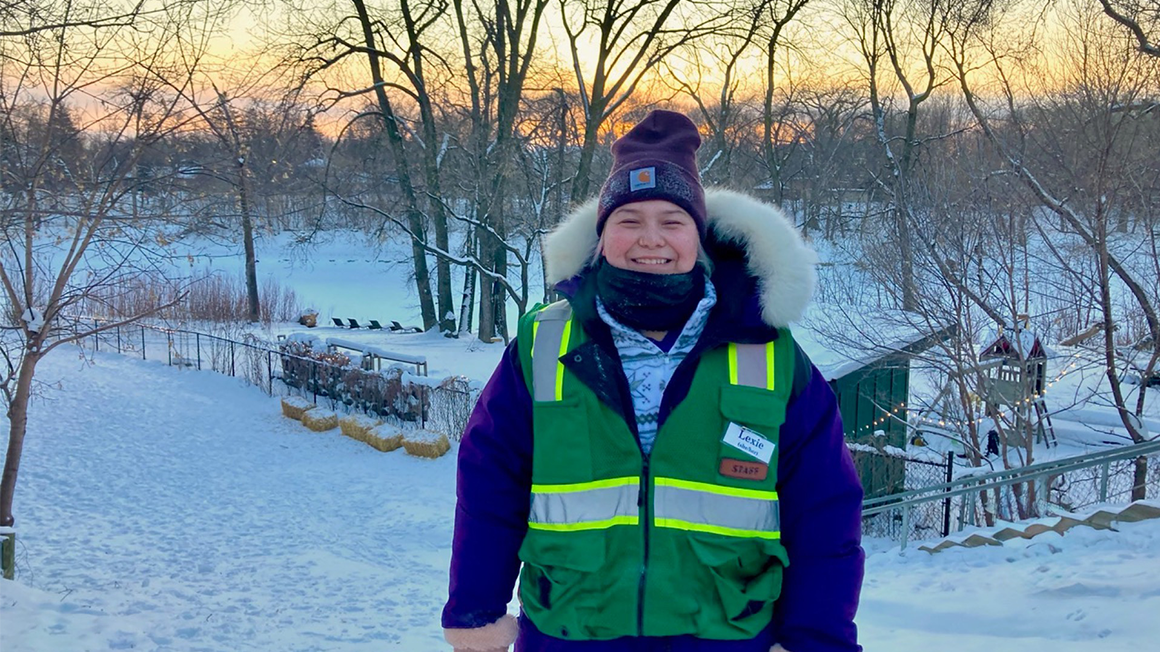 Lexie, dressed in winter clothing, posses for a photo in front of a sunset.